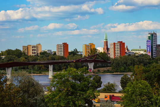 Curved pedestrian bridge over the Vistula River in Warsaw, Poland, Karowa Bridge with modern skyline and historic buildings including St. Michael the Archangel and St. Florian Cathedral