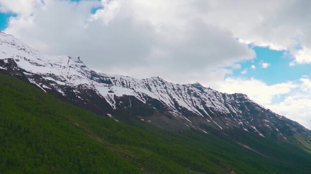 Wide angle shot of snow covered Himalayan mountain peaks with clouds above them during the summer season as seen from Sural Bhatori in Pangi Valley, Himachal Pradesh, India. Natural background.