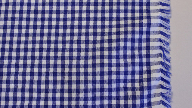  Close up of classic blue and white gingham fabric. Texture of blue plaid cotton cloth with fringed edge background.