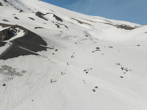 Aerial view of the south side of Mount Etna with a line of hikers trekking across the snowy volcanic landscape under a clear blue sky Nicolosi, Sicilia, Italy.