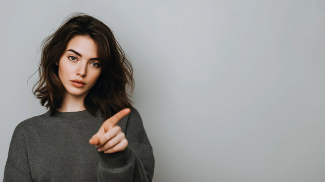 A young woman with dark, wavy hair gazes directly at the camera, her left index finger raised in a clear gesture of caution or disapproval.