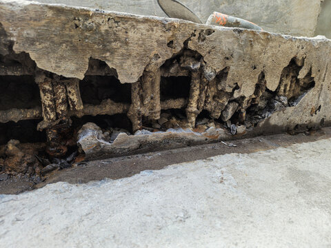 Close-up of severely damaged reinforced concrete structure with visible corroded steel rebar. Industrial building showing signs of concrete spalling and structural decay.