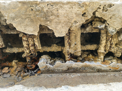 Close-up of severely damaged reinforced concrete structure with visible corroded steel rebar. Industrial building showing signs of concrete spalling and structural decay.