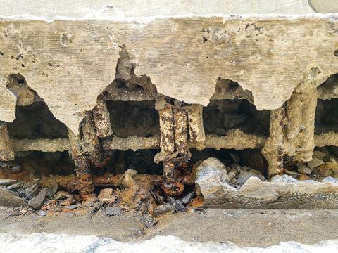 Close-up of severely damaged reinforced concrete structure with visible corroded steel rebar. Industrial building showing signs of concrete spalling and structural decay.