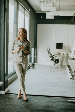 Woman in office space enjoying coffee while standing by glass wall during work hours