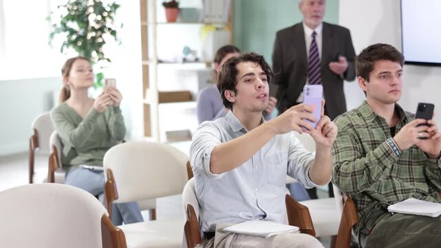  Group of young male and female students use smartphones and tablets to scan QR code or take photo in lecture hall