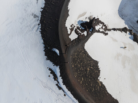 Aerial view of the snowy south slope of Mount Etna featuring dark volcanic rock and a winding path Nicolosi, Sicilia, Italy.