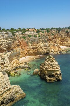 View of cliff of craggy sandstone rocks, rock formations in turquoise sea, sandy beach, Praia da Marinha, Algarve, Lagos, Portugal