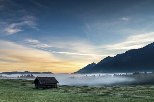 Mountain meadow with small hut with light ground fog and Karwendel massif in the background with sunrise, Kr&uuml;n, Bavaria, Germany
