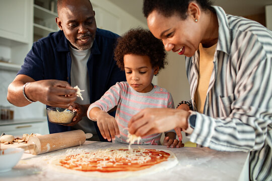 Parents and child making homemade pizza in kitchen