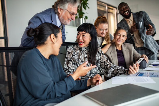 Diverse coworkers celebrating good news on smartphone in modern office