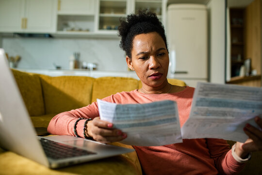 Concerned woman reviewing household bills at home with laptop