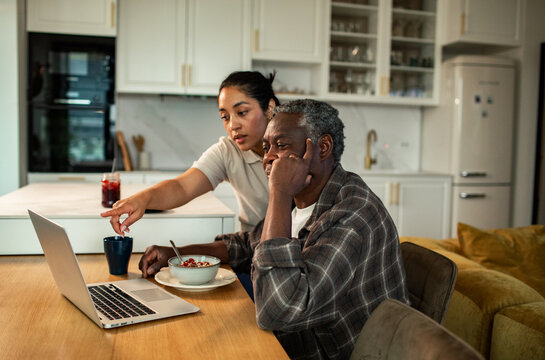Young woman helping older man with laptop in home kitchen