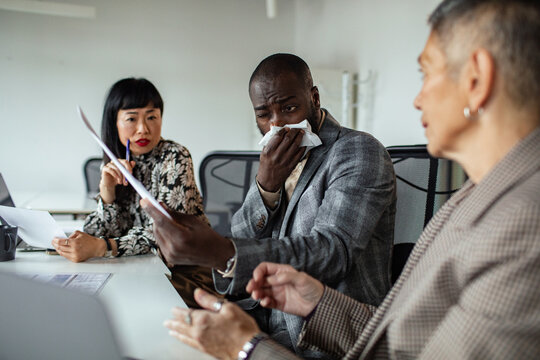 Coworkers in office meeting as man uses tissue