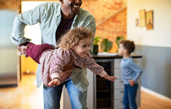 Smiling father playing airplane with daughter in home kitchen