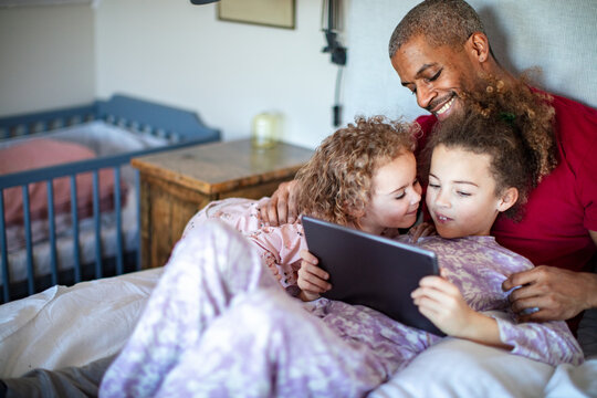 Smiling father and kids watching tablet in bedroom