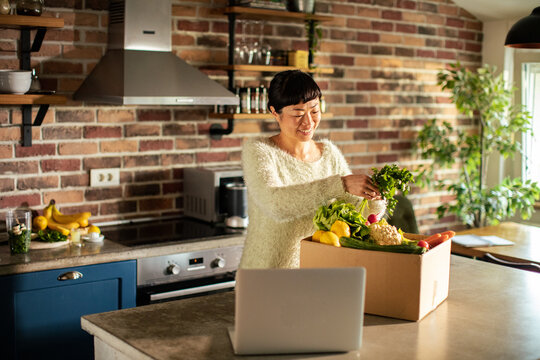 Smiling woman unpacking fresh produce delivery in home kitchen