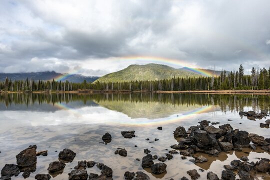 Rainbow in dark clouds over a forest, reflected in the lake, Sparks Lake, Oregon, USA