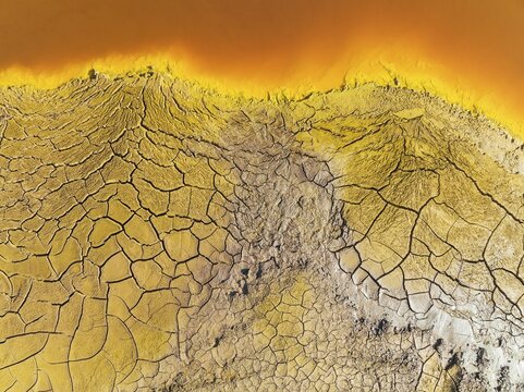 Cracked earth at the bank of the Rio Tinto (Red river) with its deep reddish hue due to oxidised iron minerals in its water, aerial view, drone shot, Huelva province, Andalusia, Spain