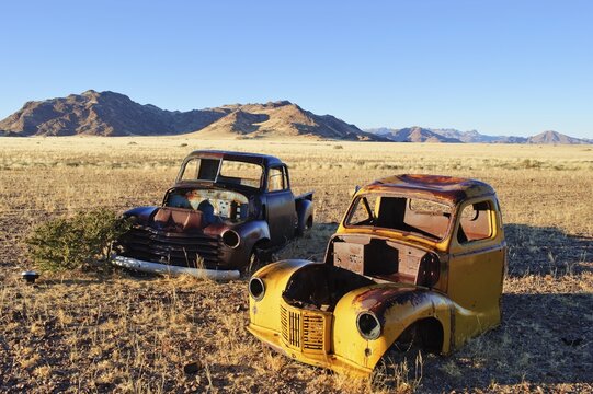 Scrap vehicles at the edge of the desert, Naukluft Mountains at back, Republic of Namibia, Africa