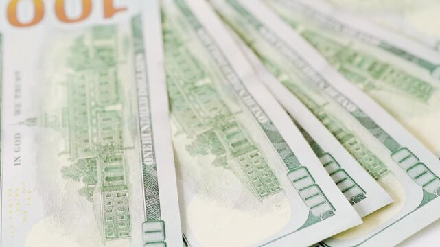 Wide fanned hundred dollar bills scattered across white surface, gusty breeze sends notes fluttering, high energy motion, risk and volatility concept for finance