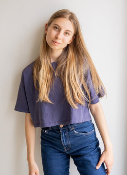 Portrait of a 12-year-old blonde pre-teen girl wearing a blue sports t-shirt and blue jeans against a white background