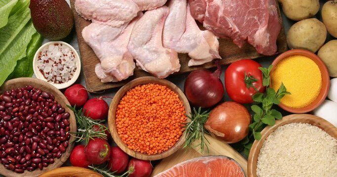 Various fresh healthy products on a gray table. Close-up footage of fish, meat, chicken, onion, radish, lettuce, mint, avocado, tomatoes, potatoes, eggs, rice, beans, lentil pasta, corn porridge.