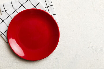 Obraz premium Top view on colored background empty round red plate on tablecloth for food. Empty dish on napkin with space for your design