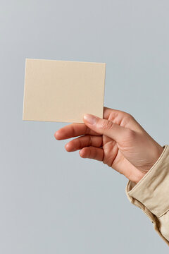 Hand holding blank textured beige paper against a light blue gray minimalist background.

