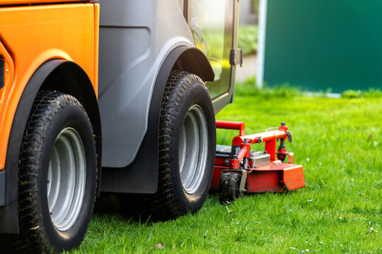 Modern ev lawn mower machine rotary cutting attachment  fresh green grass maintenance service. Closeup view wheels equipment used for landscaping care outdoor work public municipal street city park