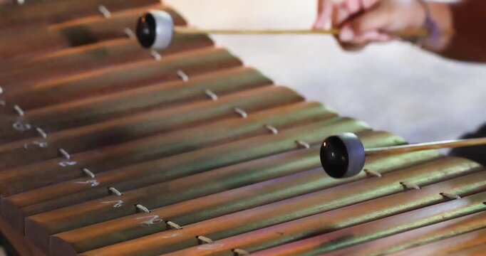Hands playing a wooden xylophone with mallets, outdoors at night market, Showcasing traditional music culture, close-up