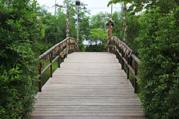 Fototapeta premium A peaceful wooden footbridge stretches across a quiet pond, flanked by lush green bushes and decorated with traditional hanging wooden tags.
