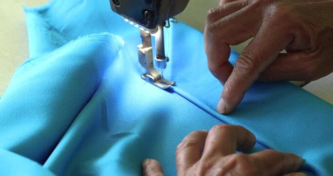 Hands sewing blue fabric with a sewing machine, close-up. Sewing machine, highlighting craftsmanship, tailoring precision, fashion production, textile industry, and handmade clothing process