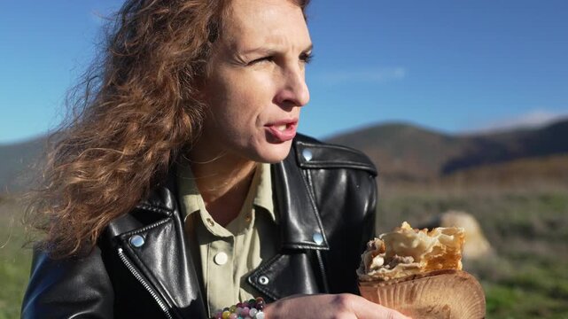 Woman, eating, outdoors, enjoying a fresh sweet snack wrapped in paper on a sunny day in the mountains.