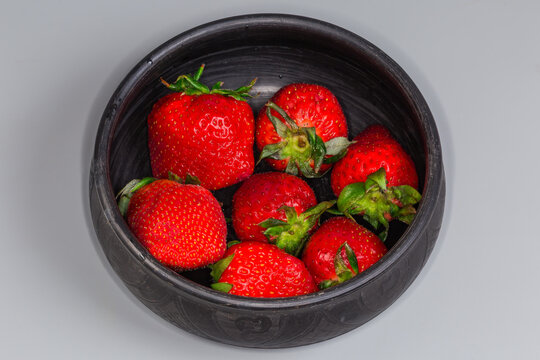 Fresh washed garden strawberries with sepals in a black bowl