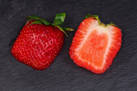 Halved fresh garden strawberry with sepal on black slate plate
