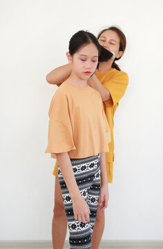Portrait of Asian mother is gently combing her cute daughter's hair against white wall background. Focus at girl kid.