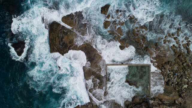 Aerial view of Newport Rock Pool with crashing waves, white foam, and turquoise water against rugged coastal rocks in Sydney, New South Wales, Australia.