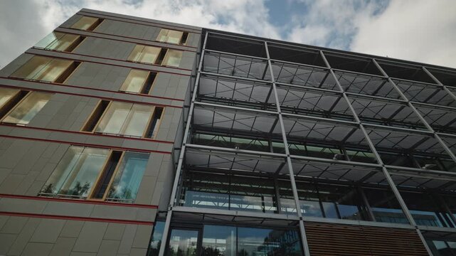 Modern office building facade with stone cladding, red accent strips and glass steel curtain wall structure, shot from below against a partly cloudy sky in Berlin, Germany.
