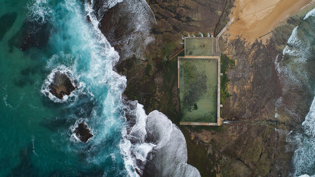 Aerial view of Newport Rock Pool with turquoise waves crashing against the rocky shore and white foam in Sydney, New South Wales, Australia.