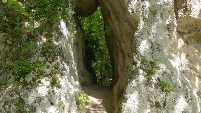 Walking towards the entrance of a limestone cave in a lush green forest, Molise, Italy