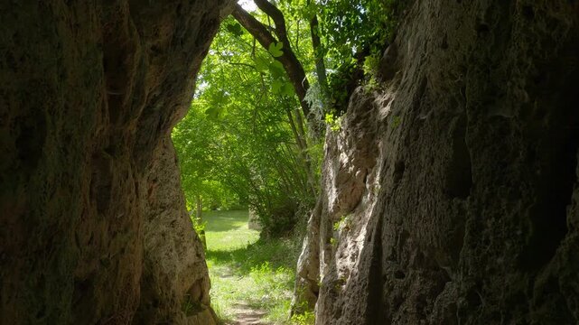 Walking towards the entrance of a limestone cave in a lush green forest, Molise, Italy