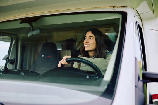 Young woman driving a recreational vehicle, smiling and looking out of the window. Representing travel, freedom, and exploration