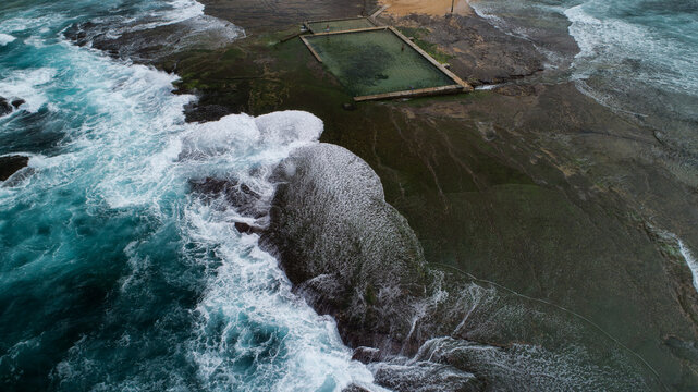 Aerial view of Newport Rock Pool with turquoise waves crashing against the rocky shore and white foam Sydney, New South Wales, Australia.