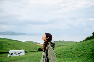 Fototapeta premium Woman standing with eyes closed, finding peace and freedom in the natural landscape near a camper van and coastline