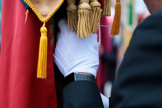 Detalle de mano con guante blanco sosteniendo una bandera ornamental con flecos dorados