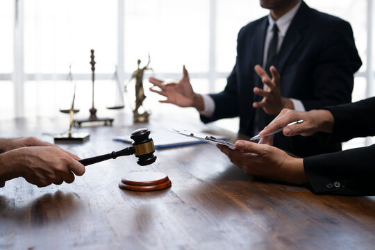 Judge holding gavel during trial in courtroom discussing with lawyer and client