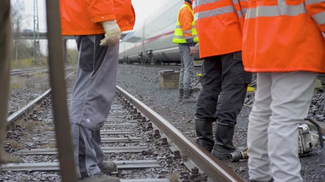 Rail Workers in Orange Safety Jackets Overseeing Passing Train on Railway Track