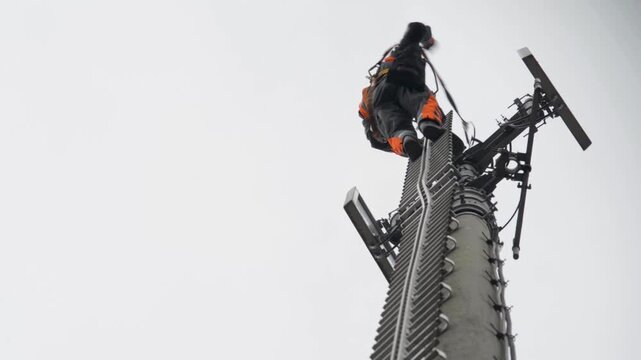 Worker Climbing Tall Communications Tower For Maintenance On Cloudy Day