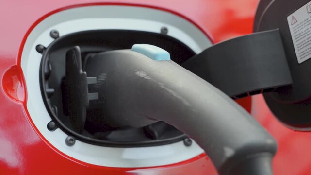 Electric Car Charging Cable Connected to Port on Red Vehicle, Clean Energy Close Up
